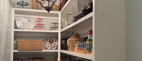 A well-organized storage room with shelves containing baskets, jars, and household items.