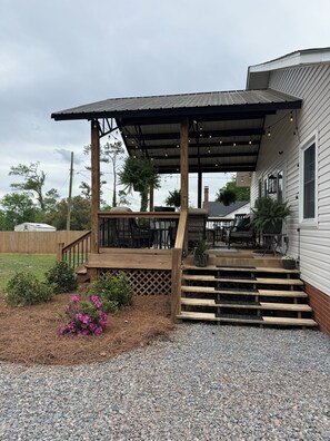 A covered outdoor seating area with wooden steps leading up to a patio, surrounded by gravel and plants.