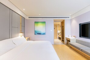 Moderni hotellihuone, jossa on suuri sänky, televisio, taulu ja erillinen vaatehuone.