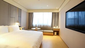 Hotelkamer met een groot bed, een zithoek met een tafel, een televisie en een raam met gordijnen.
