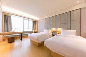 Hotellihuone, jossa on kaksi sänkyä, työpöytä ja ikkuna, jossa on verhot.