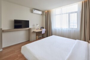 Habitación de hotel con cama, un escritorio con silla, televisión y ventana con cortinas.