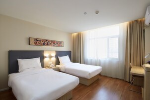 Una habitación de hotel con dos camas, una ventana con cortinas, una obra de arte en la pared y una mesita de noche con lámpara.