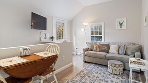A modern living room with a wooden dining table, a sofa, and a patterned rug. - Coastal Cottage in the heart of Kennebunk, ME (Kennebunk)