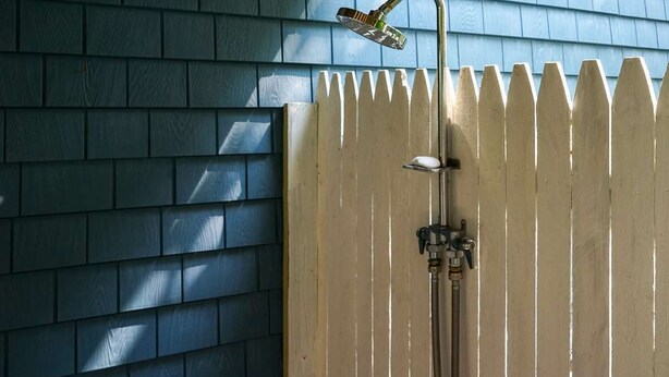 A shower with a handheld showerhead and a wall-mounted faucet, adjacent to a wooden fence. - Coastal Cottage in the heart of Kennebunk, ME (Kennebunk)