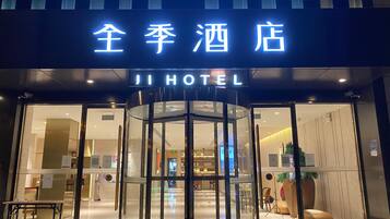 A hotel entrance with a revolving door, a sign above the door, and a visible interior with seating and a reception area.