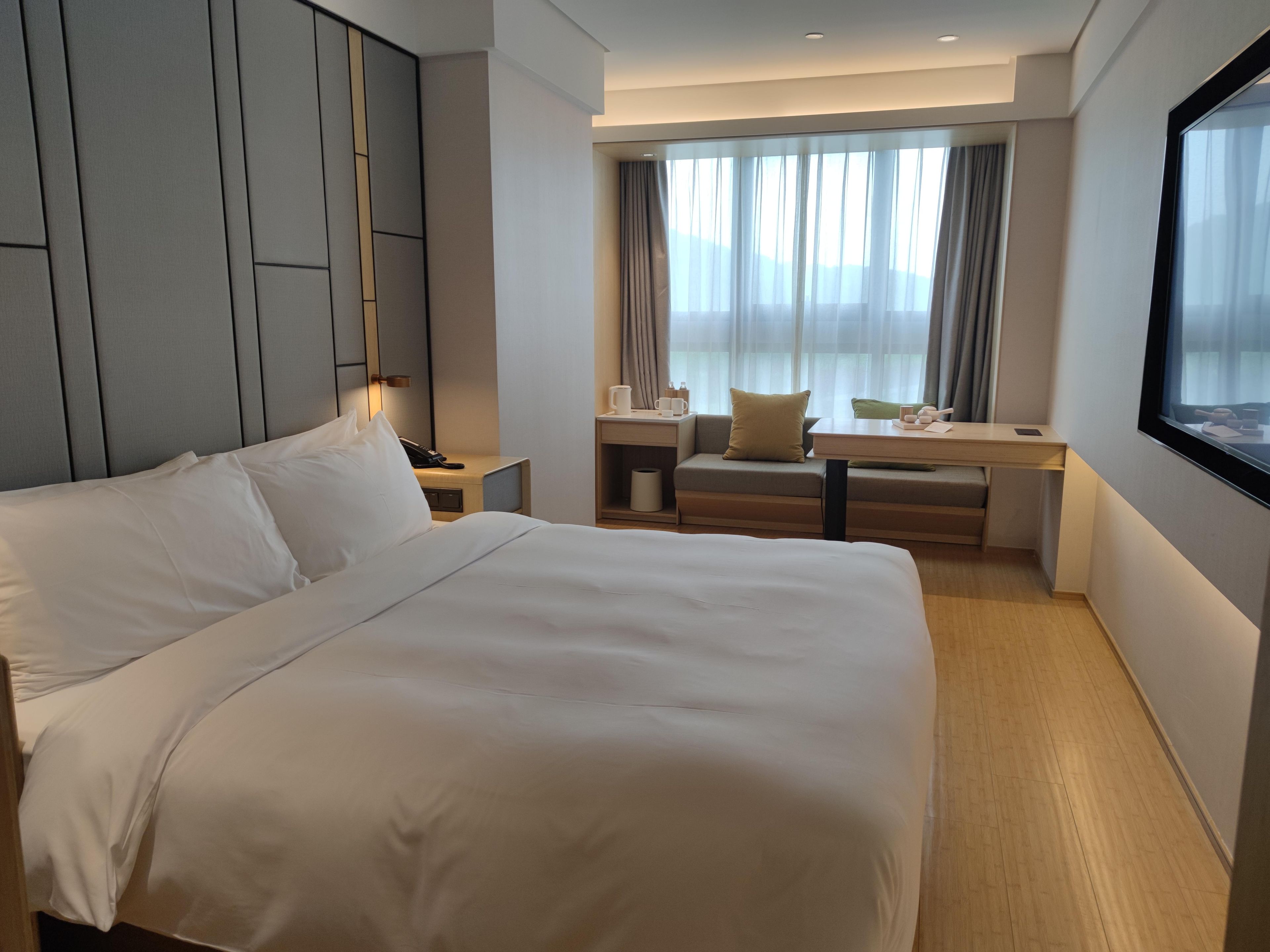 A hotel room with a large bed, a desk, and a window with curtains.