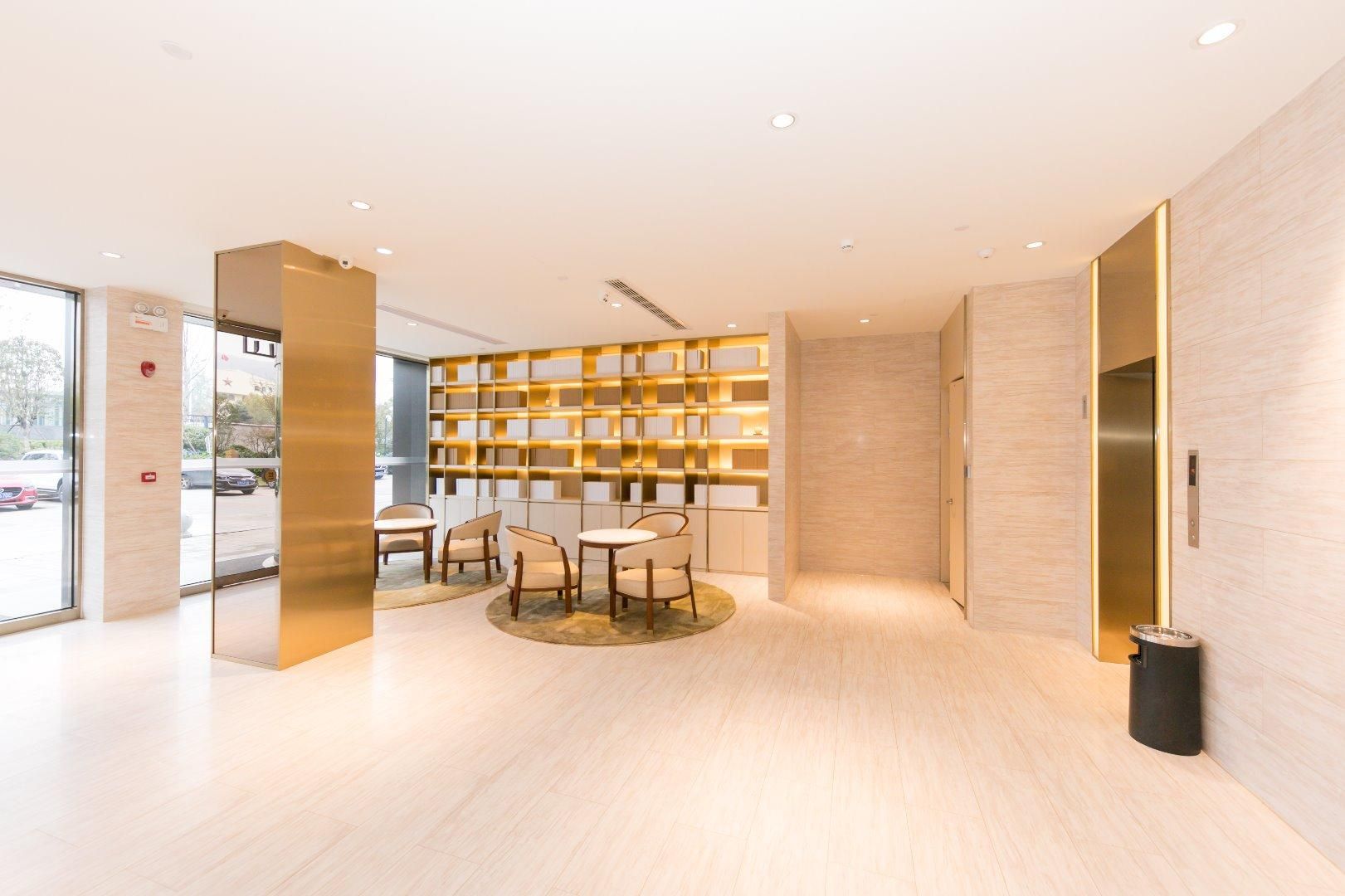 A modern lobby with a seating area, a wall-mounted bookshelf, and an elevator.