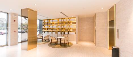 A modern lobby with a seating area, a wall-mounted bookshelf, and an elevator.