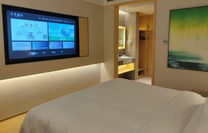 A hotel room with a bed, a TV mounted on the wall, a bathroom with a mirror, and a painting on the wall. - Ji Hotel (Hefei)