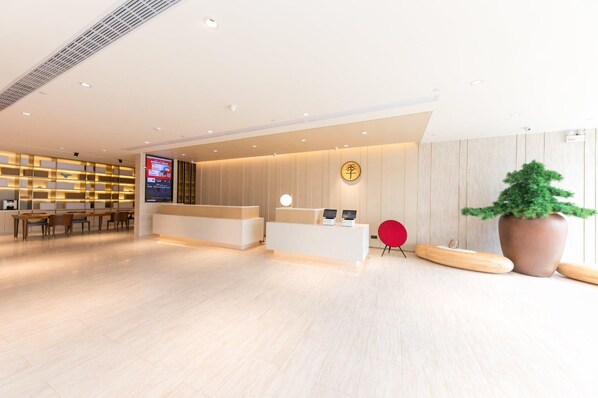 Una moderna area di ricevimento hotel con una scrivania in legno, uno schermo digitale e un'ampia pianta in vaso.