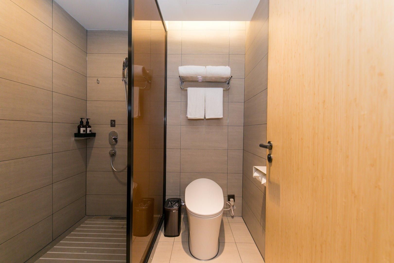 A modern bathroom with a glass shower enclosure, a toilet, and a wooden door.