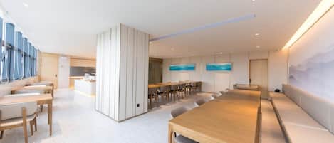 A modern conference room with a long table, several chairs, a kitchen area, and a seating area with a view.