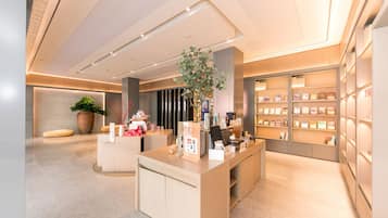 A modern, well-lit reception area with a central desk, a large potted plant, and a bookshelf filled with books and magazines.