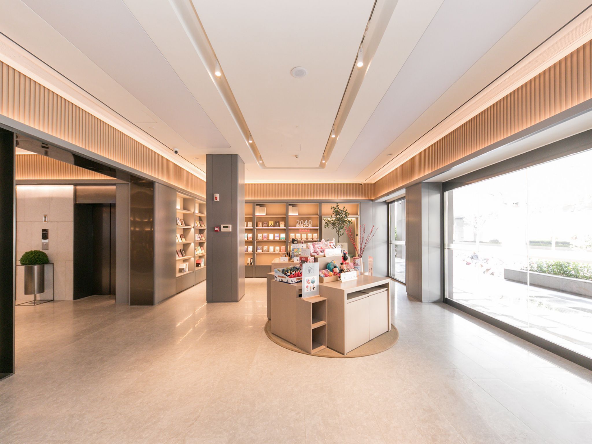 A modern interior with a central display area, bookshelves, and a large window providing a view of the outside.