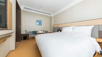 A modern hotel room with a large bed, a TV mounted on the wall, a small table with a chair, and a waste bin.