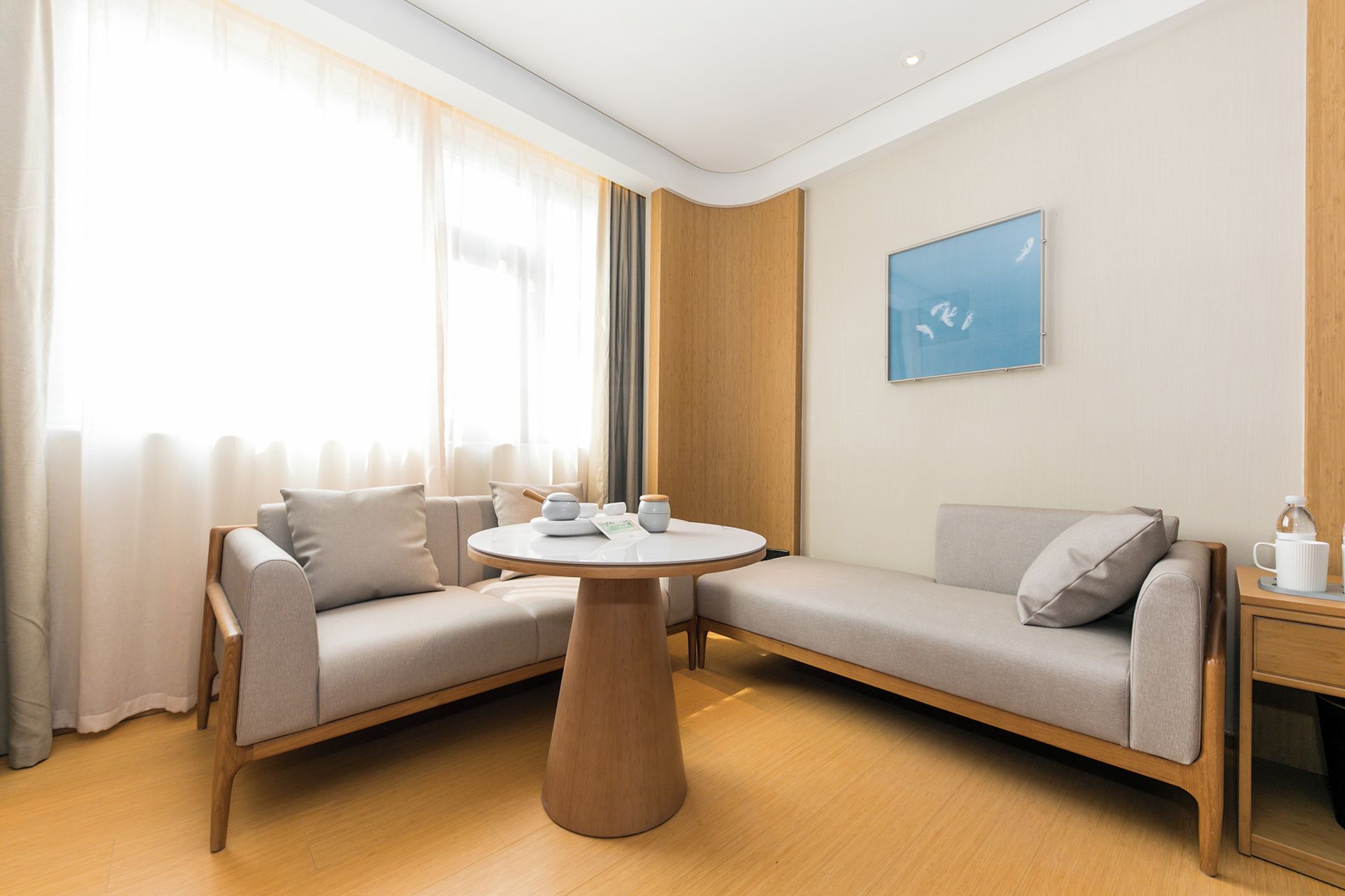 A modern hotel room with a sofa set, a round wooden table, and a painting on the wall.