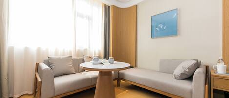 A modern hotel room with a sofa set, a round wooden table, and a painting on the wall.