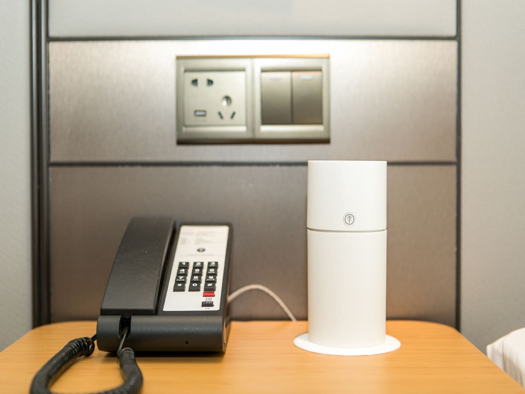 A hotel room with a telephone and a white cylindrical device on a wooden table.