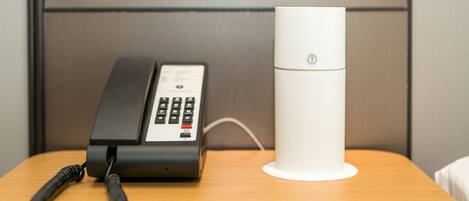 A hotel room with a telephone and a white cylindrical device on a wooden table.