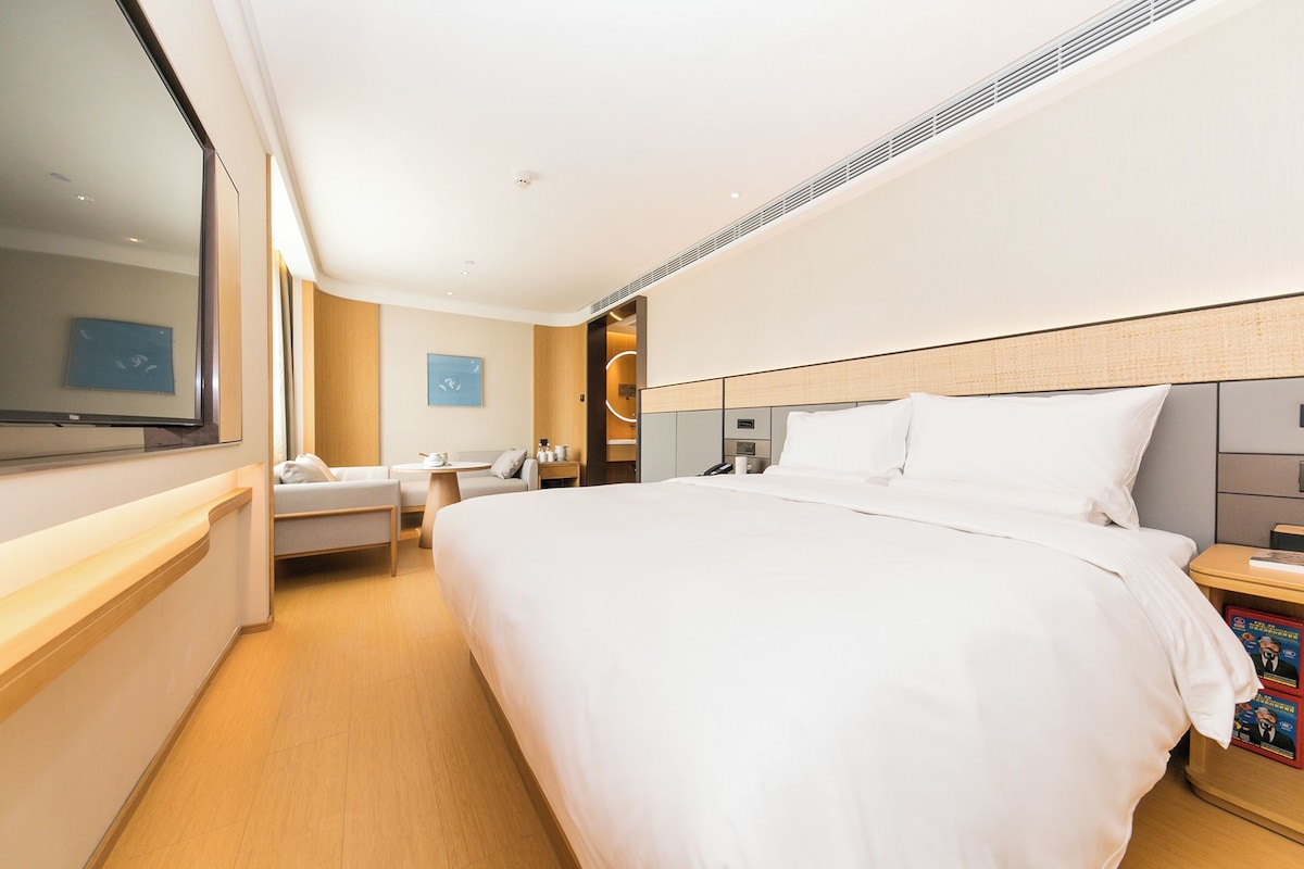 A modern hotel room with a large bed, a desk, a chair, a TV, and a small table.