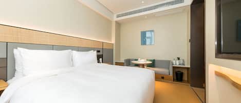 A modern hotel room with a large bed, a seating area with a table, and a TV mounted on the wall.