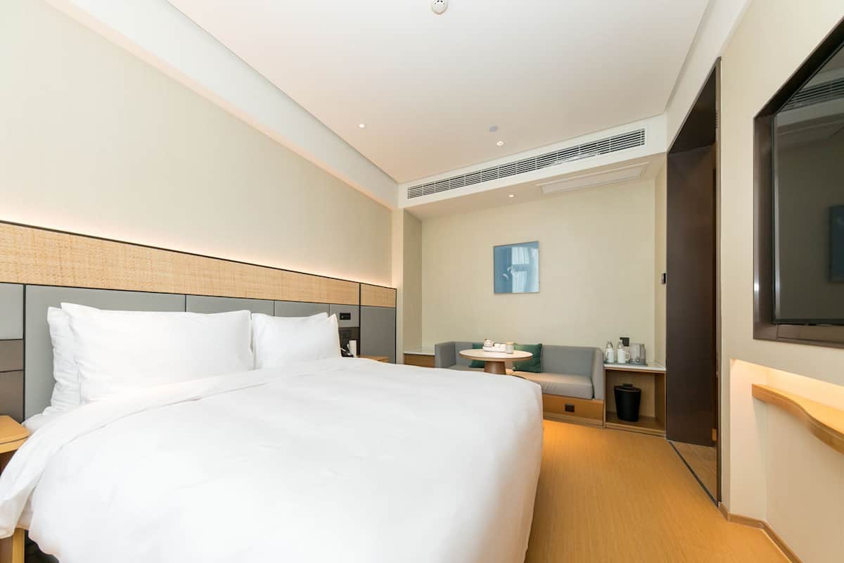 Una habitación de hotel moderna con una cama grande, un área de descanso con una mesa y un televisor en la pared.