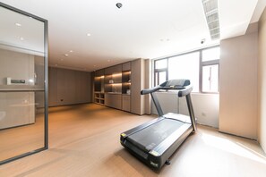 Une pièce moderne et bien éclairée, équipée d’un tapis de course, de rayonnages intégrés et de grandes fenêtres.