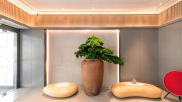 A modern lobby with a large potted plant, two wooden stools, and a red chair.