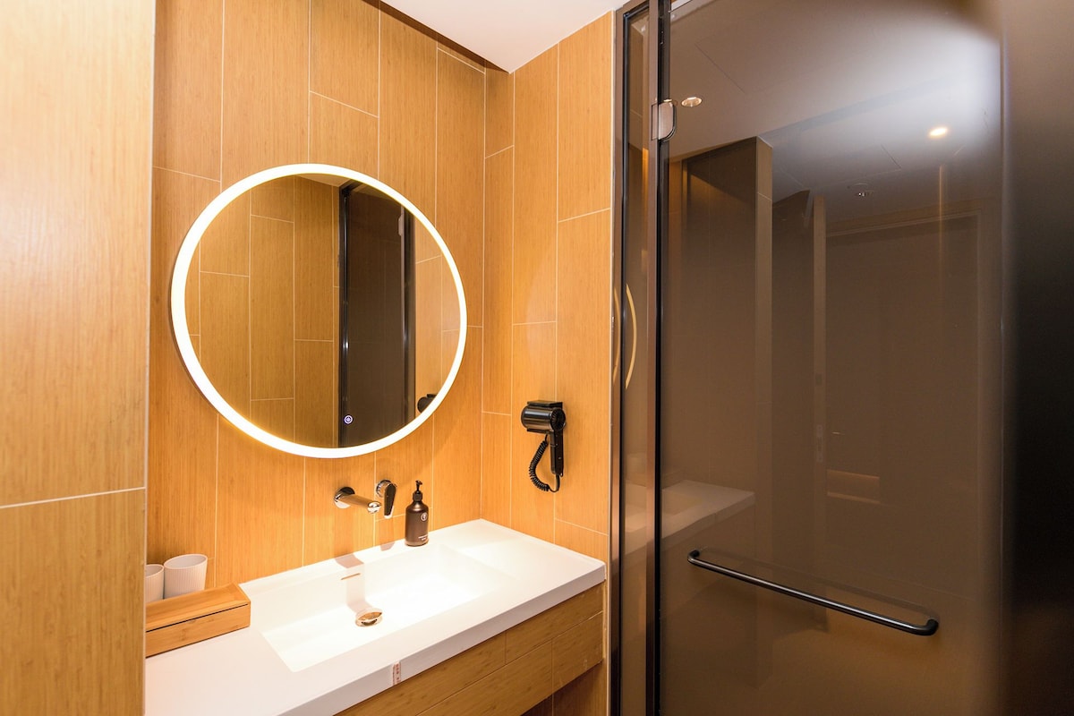 Une salle de bain moderne avec un meuble-lavabo en bois, un miroir rond, une douchette à main et une douche à parois de verre.