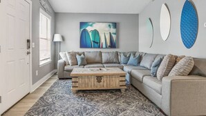 A modern living room with a sectional sofa, a coffee table, and a large abstract painting. - Completely Remodeled Beach Getaway – Walk to Beach (Panama City Beach)