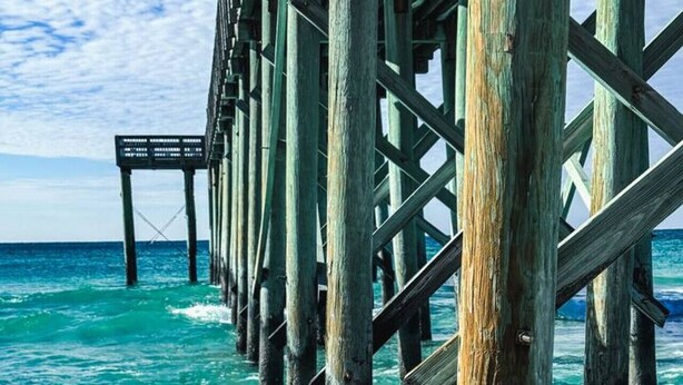 A pier extending into turquoise waters with wooden beams and a metal walkway. - Completely Remodeled Beach Getaway – Walk to Beach (Panama City Beach)
