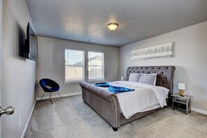 Un dormitorio con una cama grande, una silla, un televisor montado en la pared y una ventana con persianas.