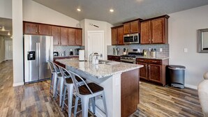 Una cocina moderna con un refrigerador de acero inoxidable, un microondas y una estufa. Hay armarios de madera y una encimera de granito.