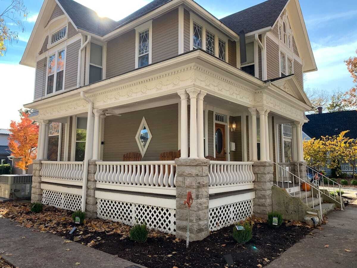 A two-story house with a front porch, stone columns, and a diamond-shaped window.