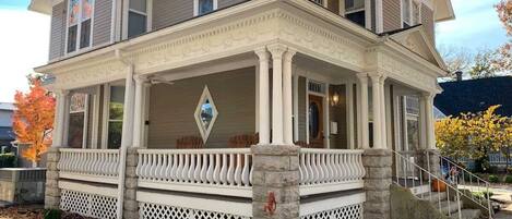 A two-story house with a front porch, stone columns, and a diamond-shaped window.