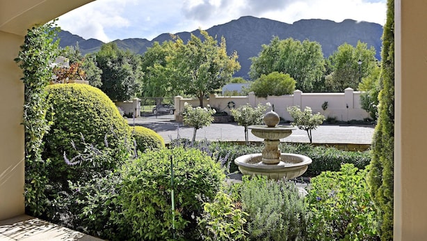 A landscaped garden with a fountain, manicured hedges, and a view of mountains. - Grande Plaisir Holiday Home (Franschhoek)