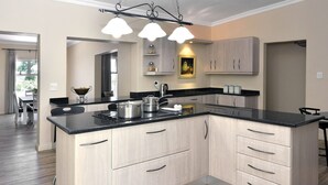 A modern kitchen with a central island, light wood cabinets, and a black countertop. - Grande Plaisir Holiday Home (Franschhoek)