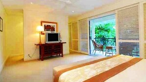 Ein Schlafzimmer mit Bett, Fernseher auf einem Schrank, einem Sessel und einem Balkon mit Rollläden.