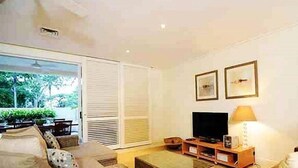 Ein Wohnzimmer mit einer Couch, einem Fernseher und einer Lampe. An der Wand hängen zwei gerahmte Bilder.
