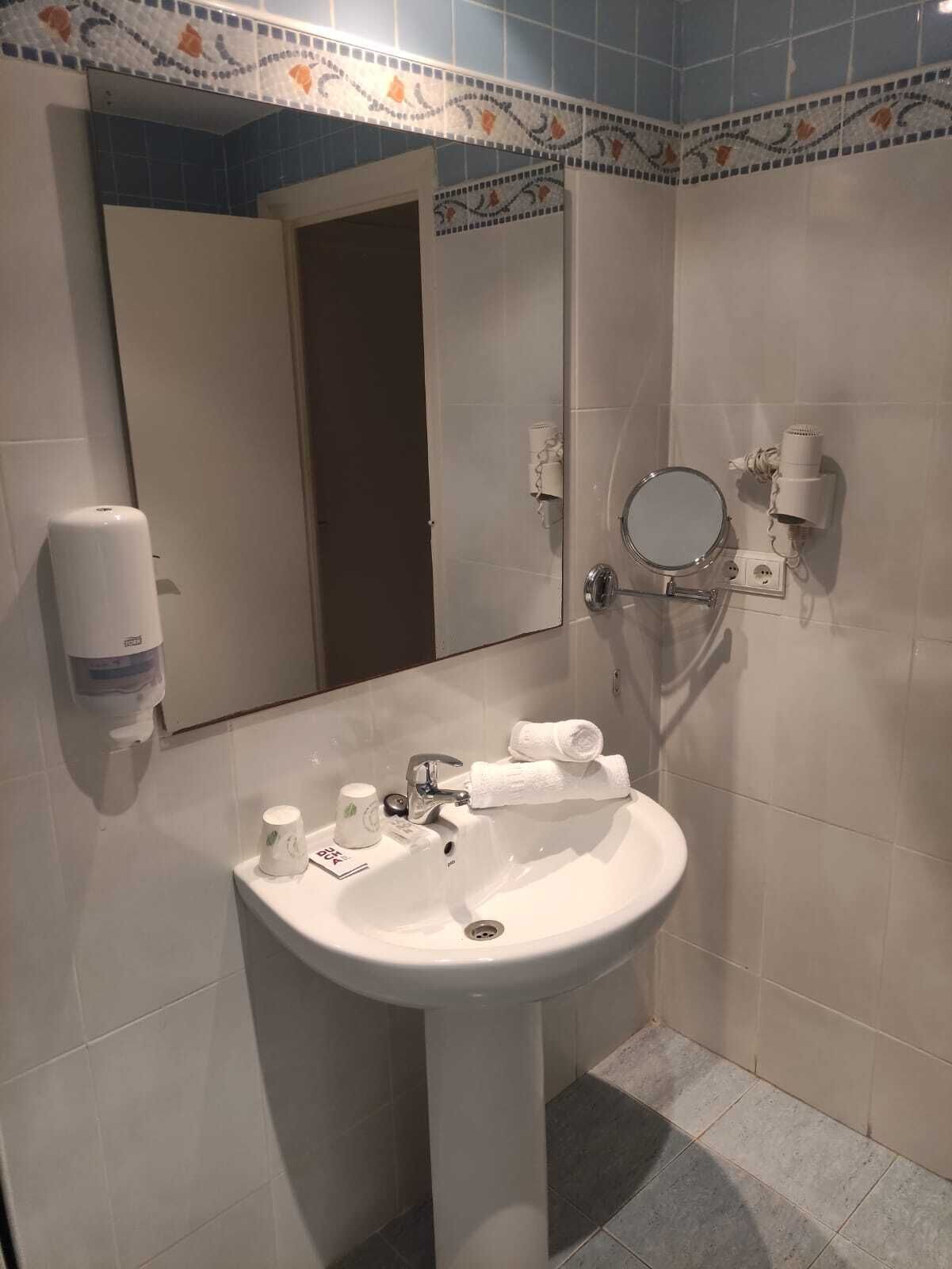 A bathroom with a white sink, a mirror, a towel rack, a hand dryer, and a soap dispenser.
