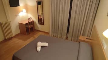 Habitación de hotel con cama, escritorio, silla, espejo y radiador.