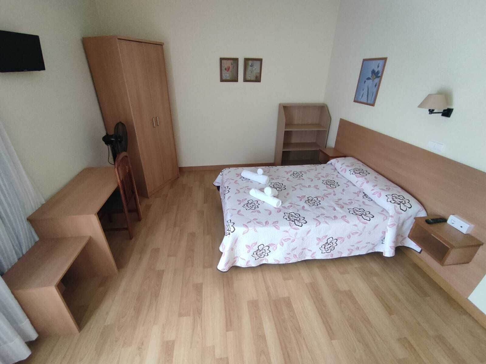 Un dormitorio pequeño con cama, armario de madera, escritorio y silla.