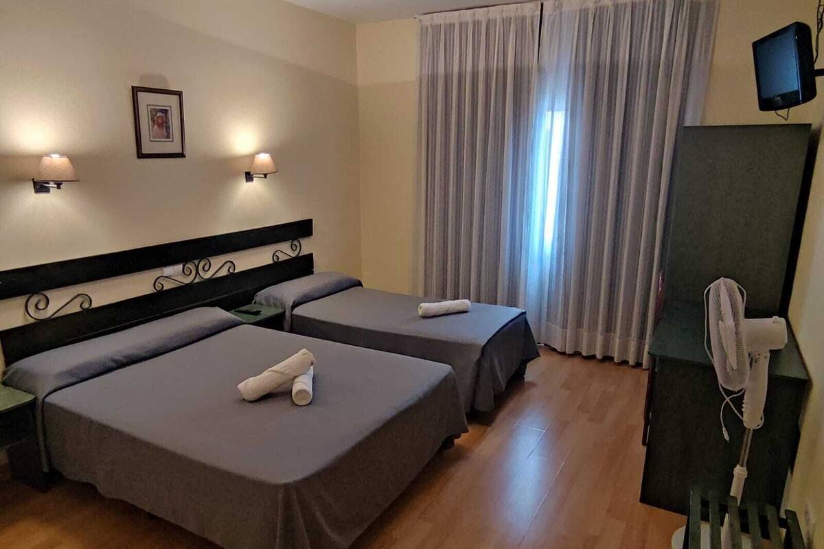 A hotel room with two beds, a desk, a chair, a television, and a window with curtains.