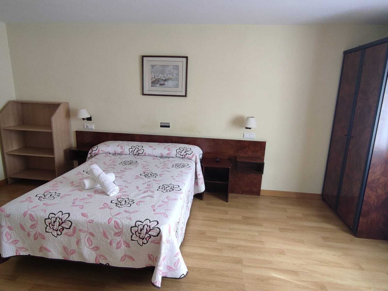 Habitació d'hotel ben ordenada amb un llit, escriptori, armari i un quadre amb marc a la paret.
