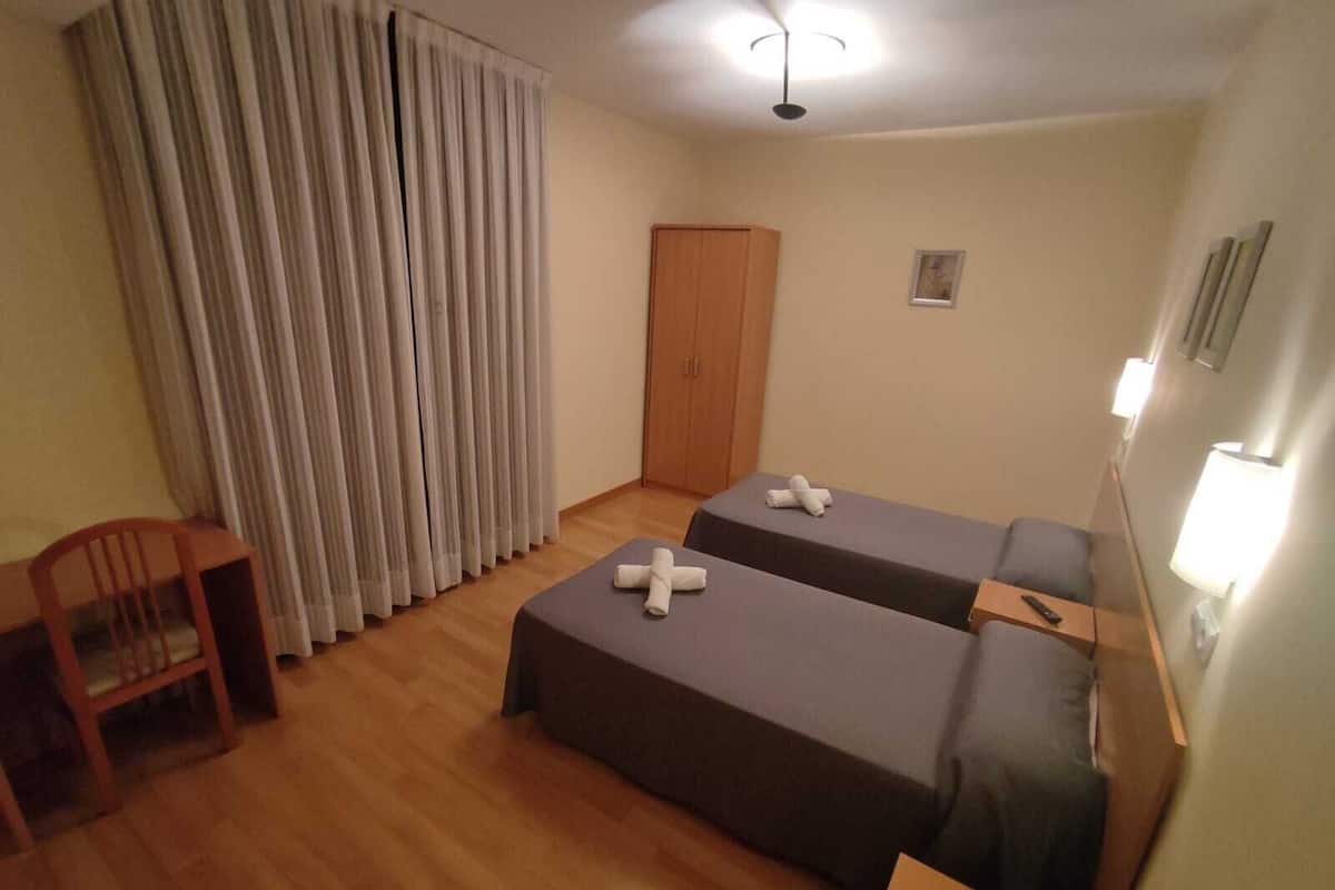 A room with two single beds, a wooden chair, a desk, a wardrobe, and a ceiling fan.