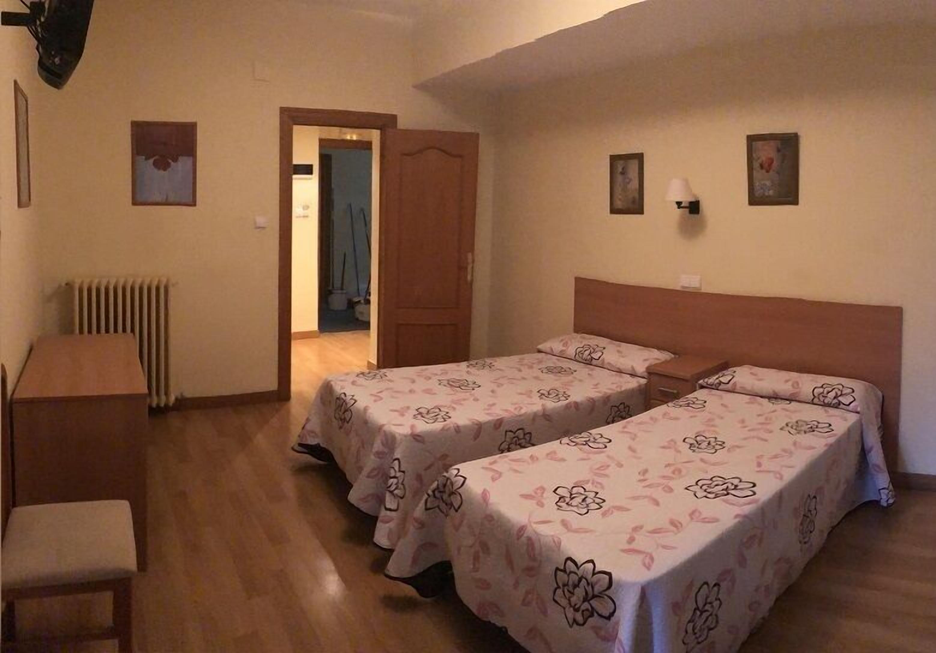 A room with two single beds, a wooden desk, a chair, and a radiator.
