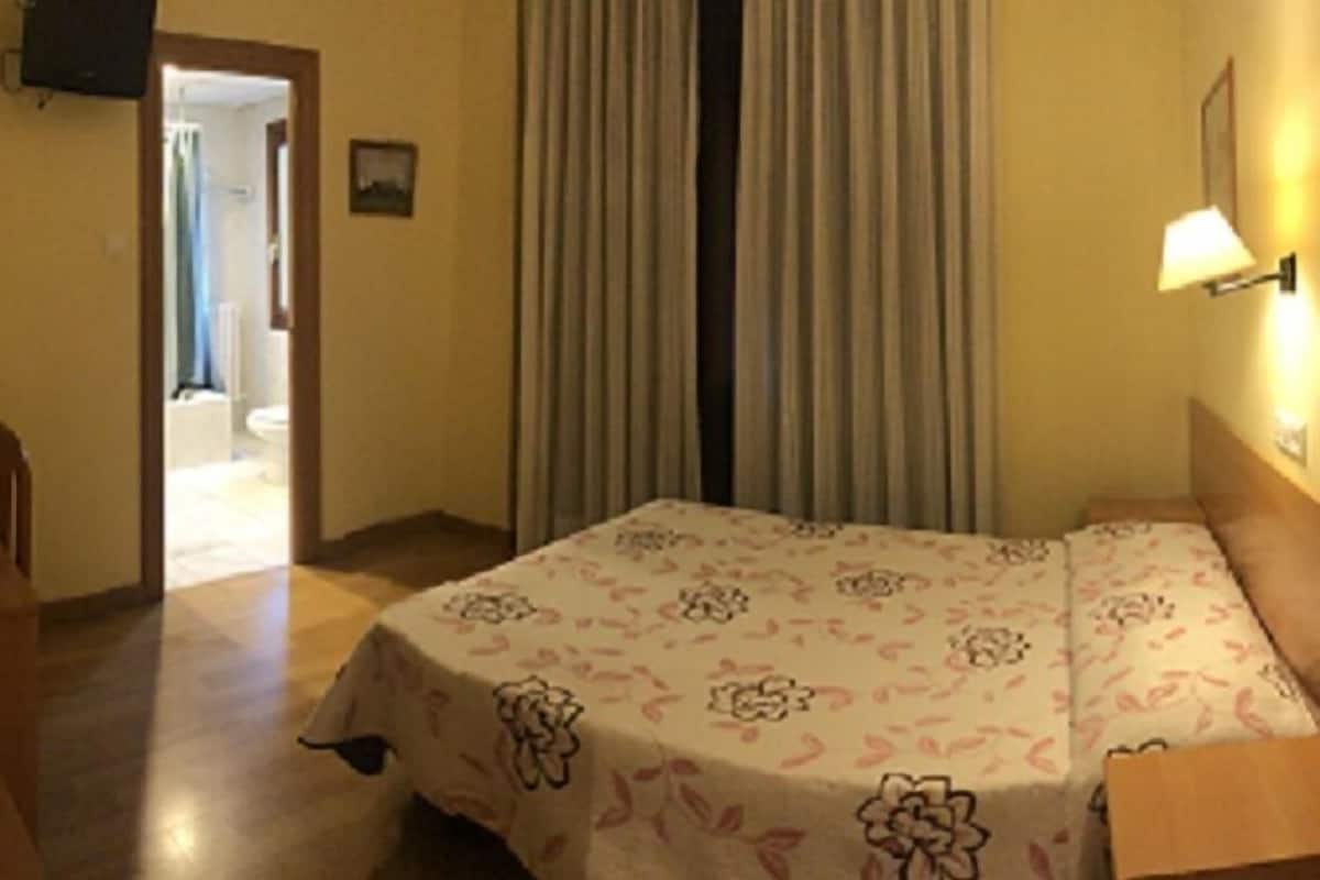A hotel room with a bed, a nightstand, a lamp, and a door leading to a bathroom.