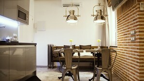 A compact kitchen with a microwave, a dining table with chairs, and a brick wall. - Suites Miguel Ángel - Adults Only (Madrid)