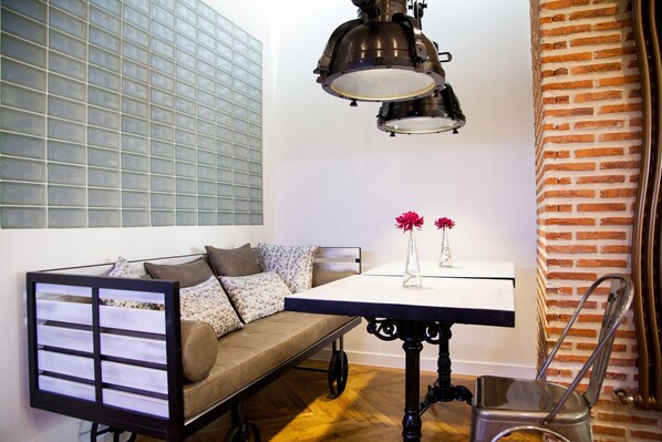 A modern living space with a sofa, a table with vases, a brick wall, and a hanging light fixture. - Suites Miguel Ángel - Adults Only (Madrid)